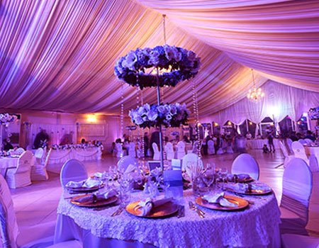 Elegant purple-lit tented reception with floral centerpieces